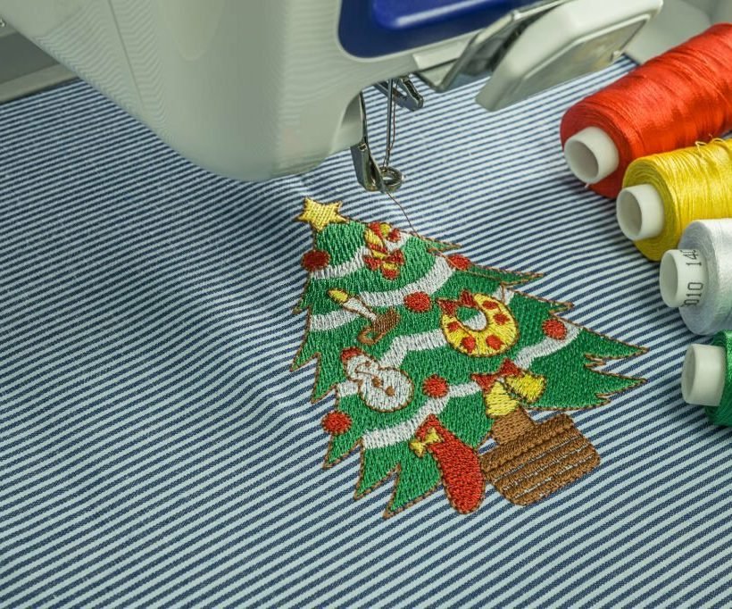 Picture of close up workspace embroidery machine finsihing work embroidered small Christmas tree and 4 color thread on white and blur cotton fabric
