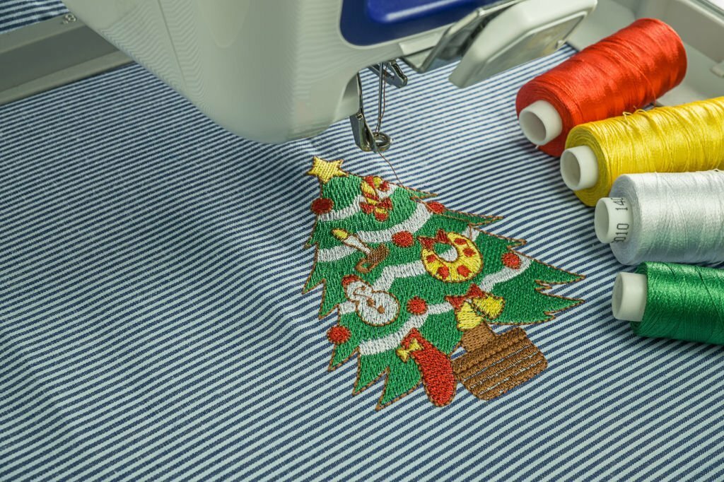 Picture of close up workspace embroidery machine finsihing work embroidered small Christmas tree and 4 color thread on white and blur cotton fabric